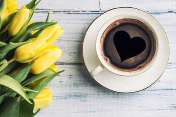 Top of view cup form coffee with heart and spring tulips on wooden table