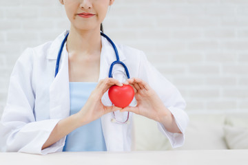 Young woman doctor holding a red heart, standing on brick wall background