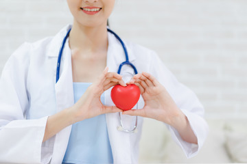 Young woman doctor holding a red heart, standing on brick wall background