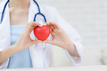 Young woman doctor holding a red heart, standing on brick wall background