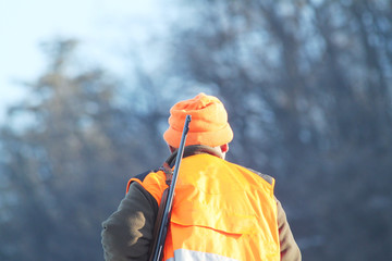Hunter with high visibility clothing and rifle, waiting for boar hunting in snowy countryside. Hunt...