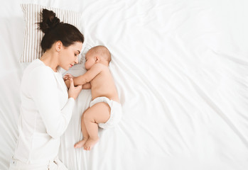 Young mom and her cute baby sleeping in bed - Powered by Adobe