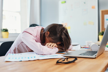 Stressed young woman resting head on desk overwhelmed by work