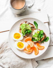 Womens cozy breakfast in bed still life - coffee, avocado sandwiches, boiled egg and tangerine on a light background, top view