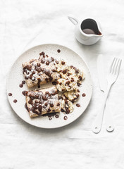 Stuffed ricotta cheese crepes with chocolate sauce, bananas and nuts on a light background, top view