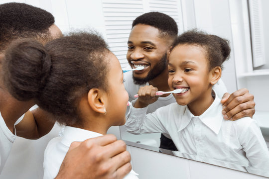 African-american girl brushing teeth together with dad