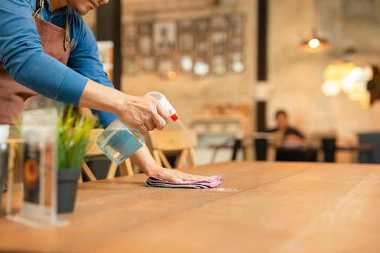 Waiter cleaning the table with spray disinfectant on table in restaurant. 