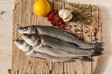 Sea bass fish with garlic, rosemary, tomatos and lemon on a wood table from above