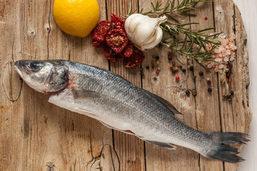 Sea bass fish with garlic, rosemary, tomatos and lemon on a wood table from above