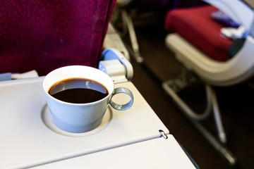 Cup of hot black coffee on table in plane cabin