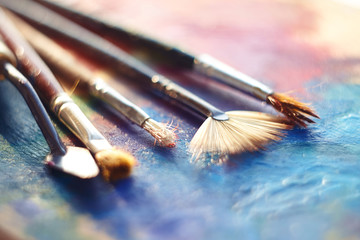 Fototapeta premium Drawing tools lie on a wooden palette, painted with multi-colored oil, illuminated by the sun