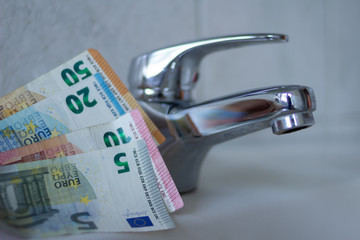 Hintergrund von Geld und Wasserhahn im Badezimmer als Symbol für Verbrauch und Wasserkosten