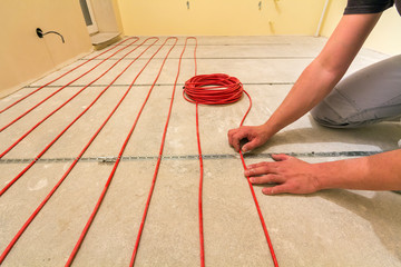 Electrician installing heating red electrical cable wire on cement floor in unfinished room. Renovation and construction, comfortable warm home concept.