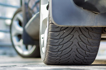 Back view detail part of black shiny luxurious car tire parked on pavement background on bright...