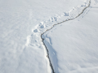 Aerial view of snow covered plain with brook flowing in straight line through landscape.