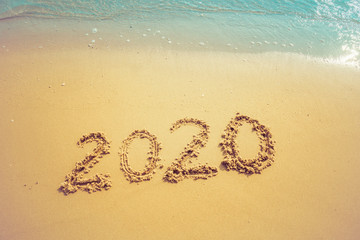 Happy New Year 2020 concept, 2020 number lettering on the sea beach, wave and golden light of sunset.