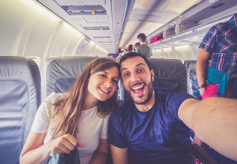 Fototapeta na wymiar Young handsome couple taking a selfie on the airplane during flight around the world. They are a man and a woman, smiling and looking at camera. Travel, happiness and lifestyle concepts.