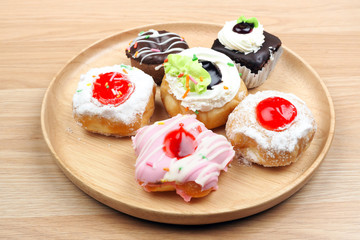 Beautiful donuts with strawberry jam and cupcake in wood dish on wooden background, bakery