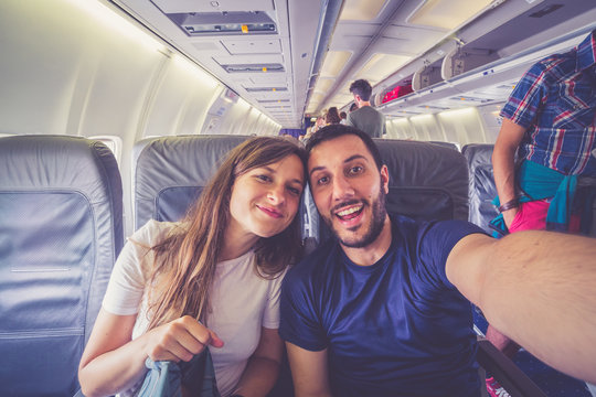 Young handsome couple taking a selfie on the airplane during flight around the world. They are a man and a woman, smiling and looking at camera. Travel, happiness and lifestyle concepts.