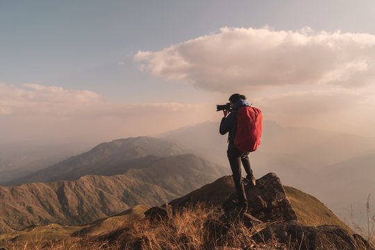 Young man traveler with backpack taking a photo on mountain, Adventure travel lifestyle concept