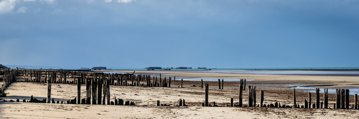 the normandy beaches in france showing ruins and relics from world war II on golden sands and dark blue waters