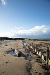 the normandy beaches in france showing ruins and relics from world war II on golden sands and dark blue waters