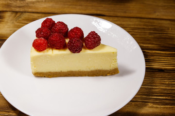 Piece of tasty New York cheesecake with raspberries in a white plate on wooden table