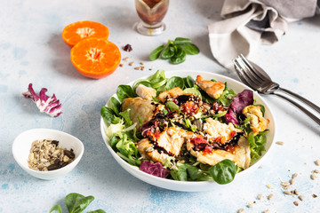 Salad mix with grilled turkey or chicken, seeds and citrus dressing on a white plate. Light concrete background. Healthy lunch or dinner. Copy space.