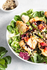 Salad mix with grilled turkey or chicken, seeds and citrus dressing on a white plate. Light concrete background. Healthy lunch or dinner. Copy space.