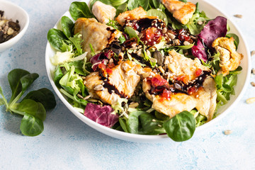 Salad mix with grilled turkey or chicken, seeds and citrus dressing on a white plate. Light concrete background. Healthy lunch or dinner. Copy space.
