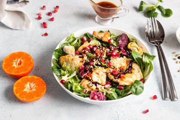 Salad mix with grilled turkey or chicken, seeds and citrus dressing on a white plate. Light concrete background. Healthy lunch or dinner. Copy space.