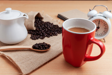 Red coffee cup with coffee beans and white alarm clock on business table