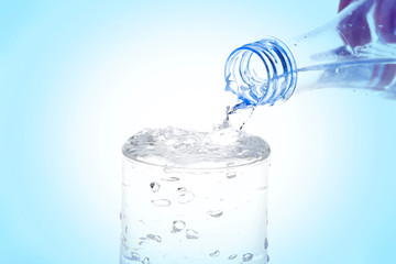 Pouring water from bottle into glass on blue background