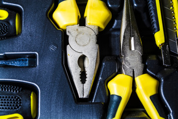 Big tool kit of black and yellow colors for the house in a box. Flat-nose pliers, screw-drivers, stationery knife and nippers. 