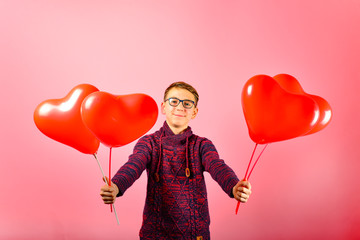 Fototapeta na wymiar A young and handsome guy gives balloons in the shape of a heart on a pink background.