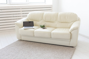 Business and interior concept - view of a white living room with sofa, an open laptop computer, home interior