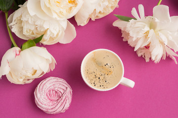 on a pink background, a cup of coffee and a homemade pink marshmallow surrounded by white peony flowers. concept