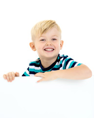 A little boy is looking from behind an empty banner.