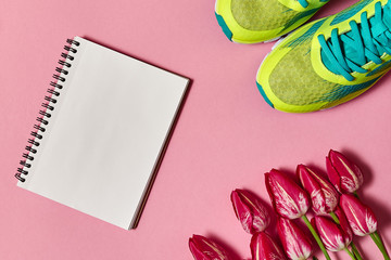 Spring sport composition with running sneakers, red tulips and open blank notebook on pink pastel background, copy space. Healthy lifestyle, sports concept. Top view, flat lay