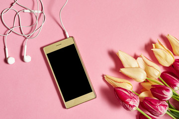 Tulips and mobile cellphone with earphones on pink pastel background, copy space. Spring minimal concept. Womens Day, Mothers Day, Valentine's Day. Nature background. Flat lay, top view