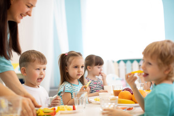 Obraz na płótnie Canvas Kids and carer together eat fruits and vegetables in kindergarten or daycare