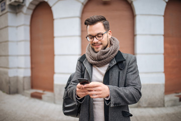 Hipster man walking in the city and typing sms.