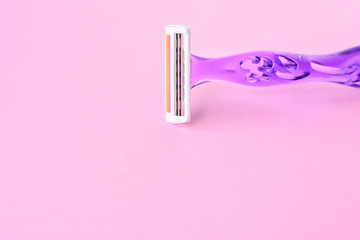 New disposable plastic violet razor with steel blade for daily safety personal shaving on pink neutral background with empty space for text. Design plastic woman shaving razor with selective focus. 