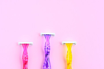 Three woman colorful razors with selective focus on neutral background. New disposable plastic razor with steel blade for daily safety personal shaving on pink background with empty space for text.