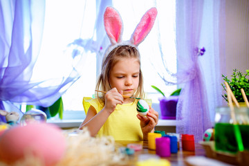 colorful painted eggs, flowers in vase. Happy easter girl in bunny ears having fun and painting eggs. small child at home. spring holiday