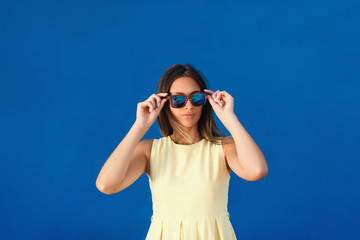 Portrait of beautiful Caucasian girl in light yellow dress putting on sunglasses while standing in...