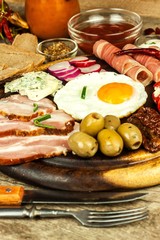 Fried egg on a wooden board. A hearty breakfast with ham and vegetables. Eggs and ham.
