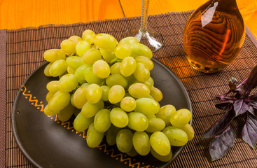 large brush of green grapes in a ceramic plate, a decanter and a glass of wine and cheese