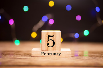 February 5th. Day 5 of february month set on wooden calendar at center of dark background with garland bokeh. Winter time. Empty space for text, mockup.
