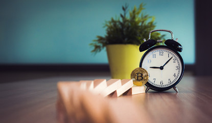 Golden bitcoin cryptocurrency beside alarm clock with dominoes falling on the table., Business financial and banking bitcoin concept.